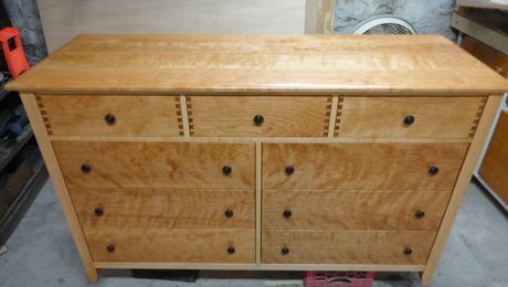 A wooden dresser with lots of drawers is sitting on a concrete floor.