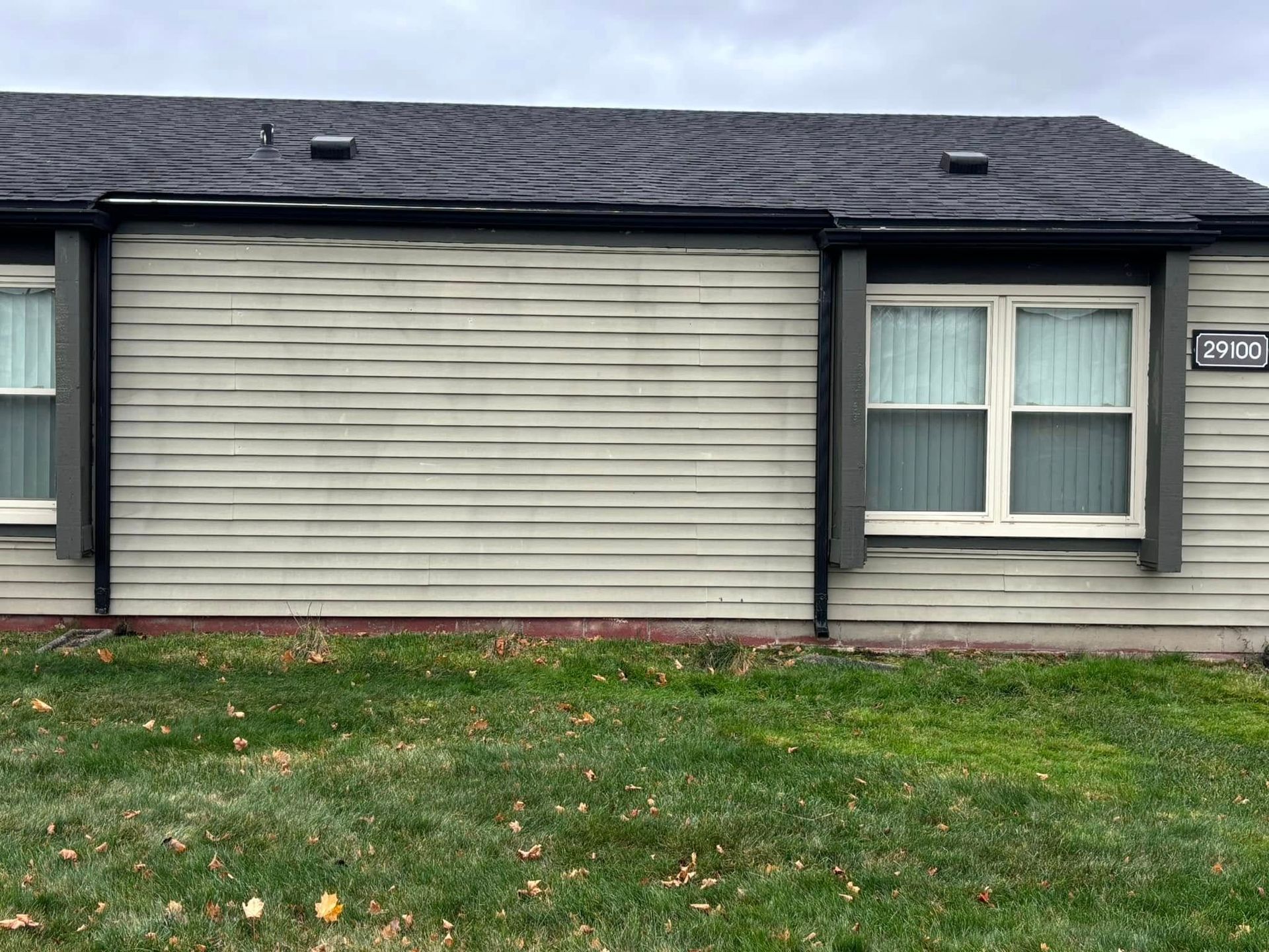 A house with a gray siding and white windows is sitting on top of a lush green lawn.