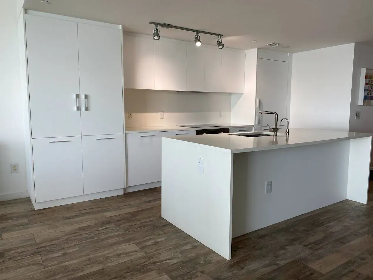A kitchen with remodel with cabinets refacing.
white kitchen cabinets and a large island in the middle | Midtown, Miami