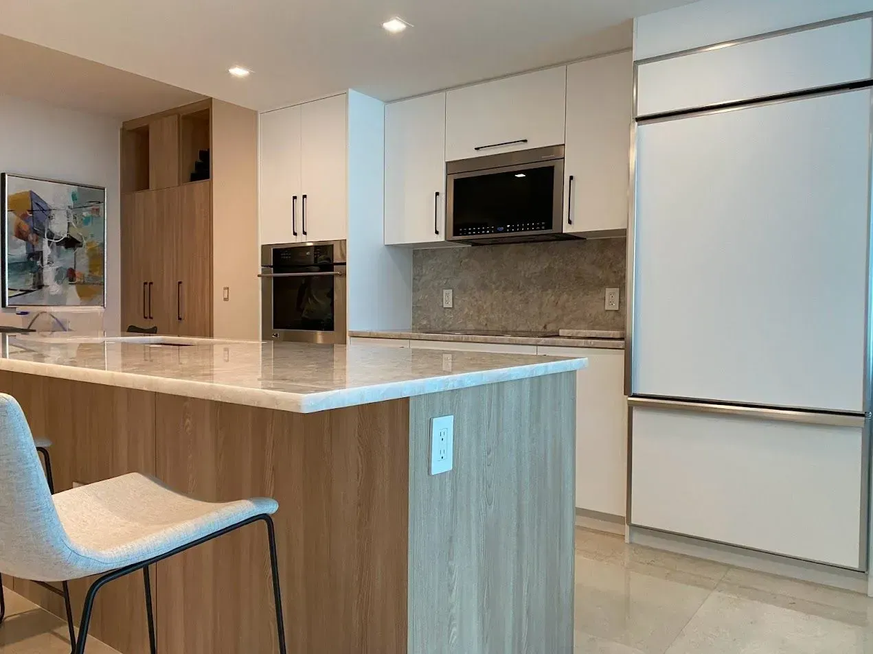 A kitchen with white cabinets , stainless steel appliances , a large island and a chair.
