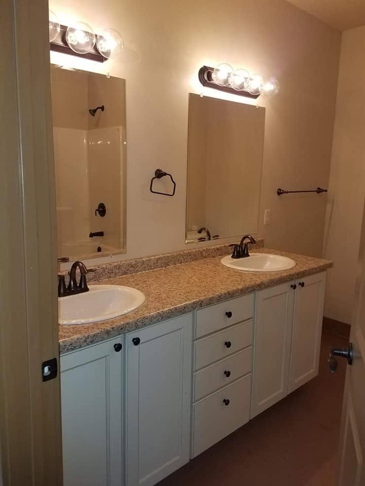 Bathroom vanity with two sinks, granite countertop, mirrors, and lights above.
