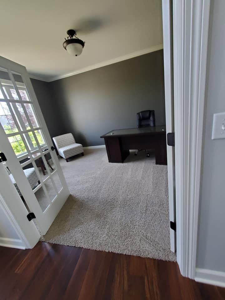 Home office with dark desk, chair, and gray walls, viewed through open French doors from a hardwood hallway