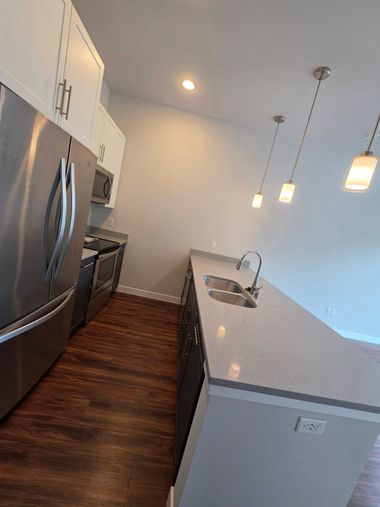 Modern kitchen with stainless steel fridge, wood floor, island sink, and pendant lights