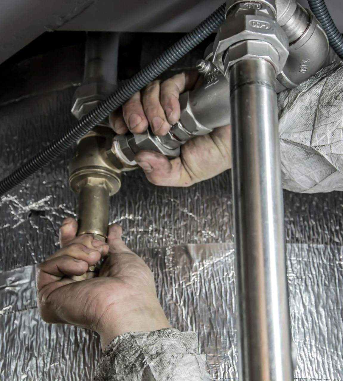 A person is fixing a pipe under a sink.