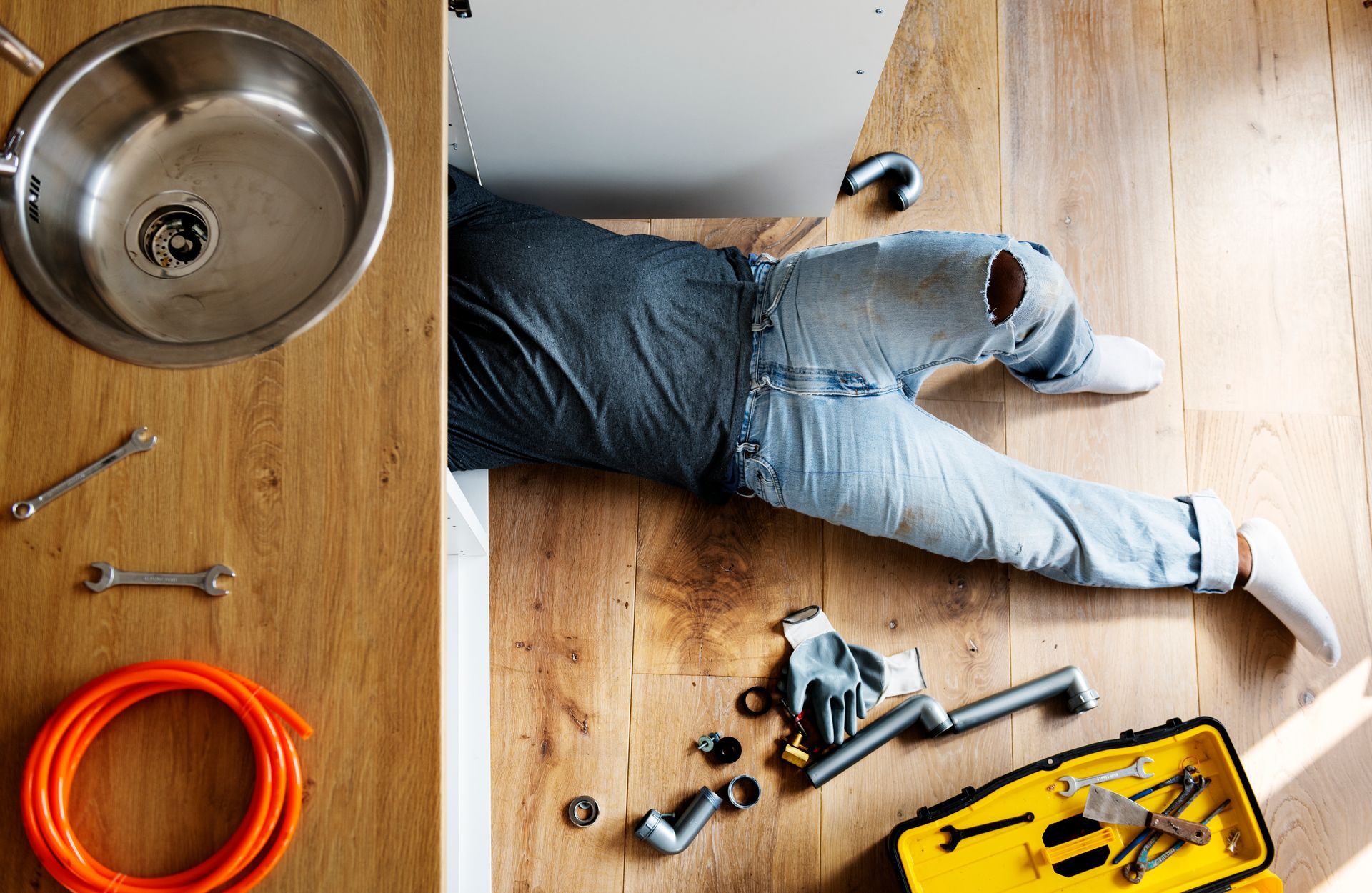 A man is laying on the floor under a sink.