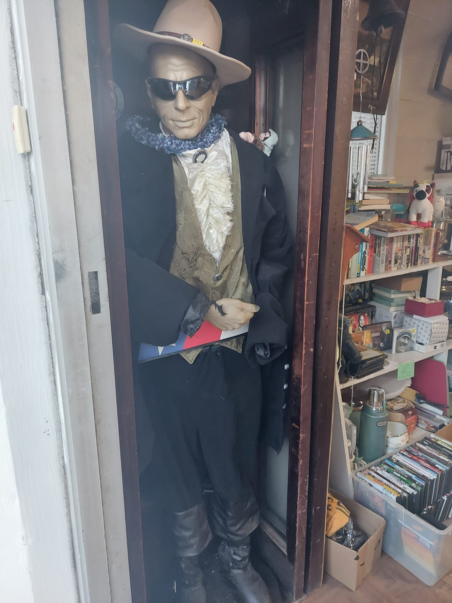 A mannequin wearing a cowboy hat and sunglasses is standing in a doorway.