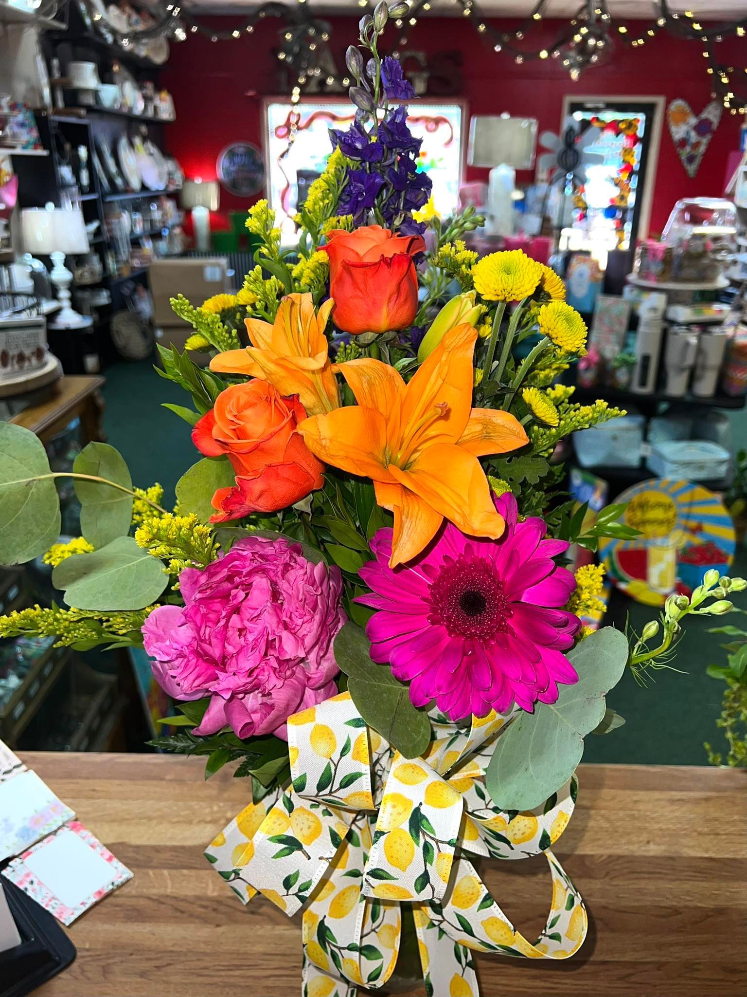 Bright floral arrangement with pink, orange, and yellow flowers, tied with a lemon-patterned bow.