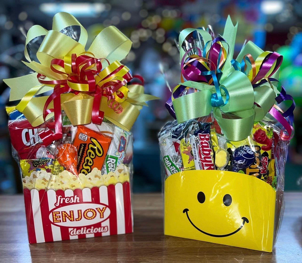 Two snack gift baskets, one popcorn box-shaped and the other a yellow smiley face, both topped with bows.