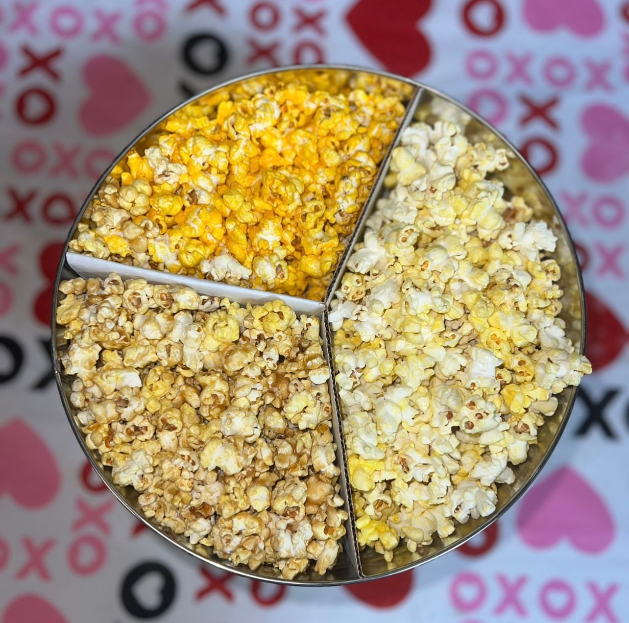 A round container divided into four sections, filled with different flavored popcorn.