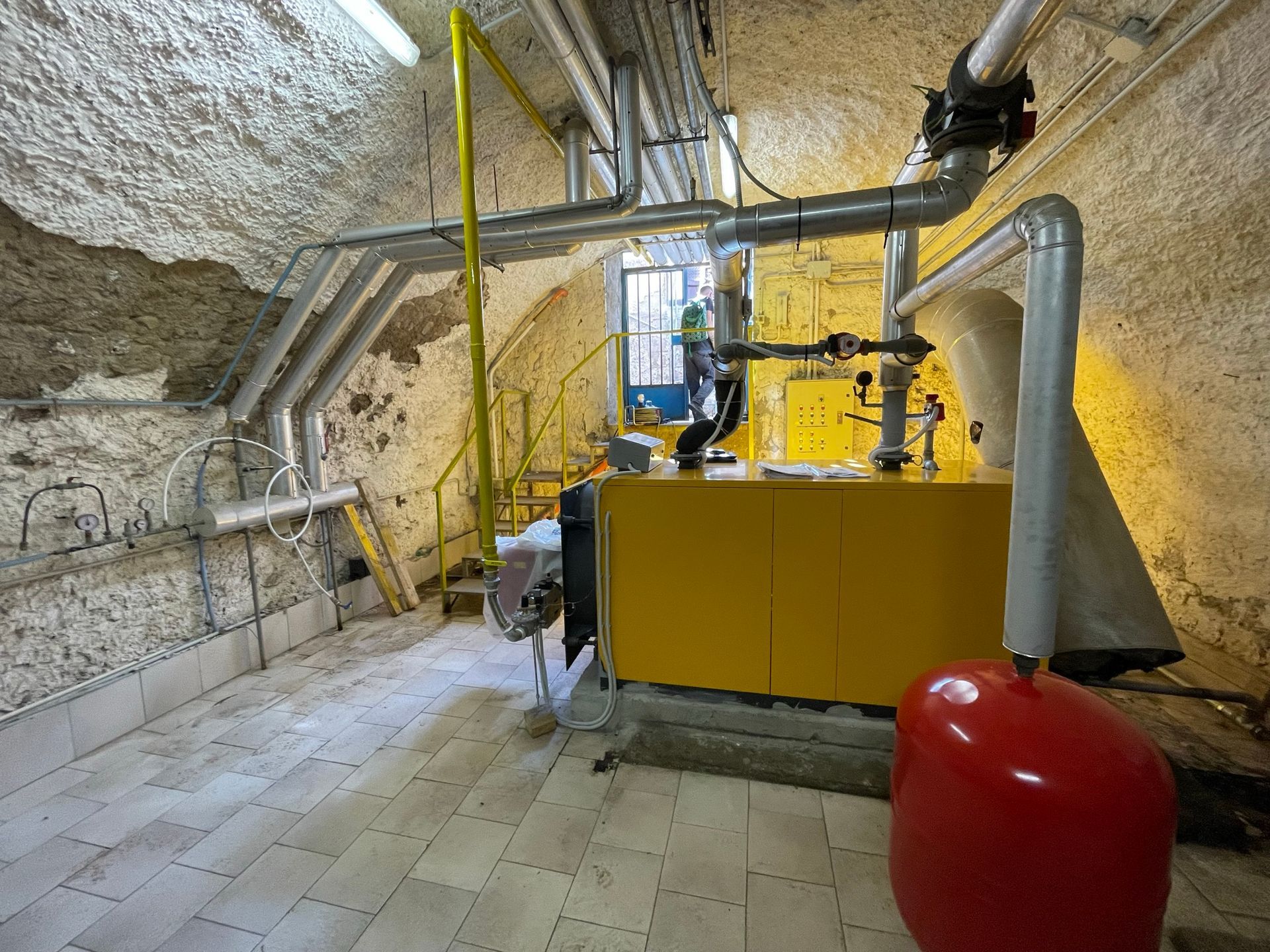 Una caldaia gialla è posizionata in una stanza accanto a un serbatoio rosso.