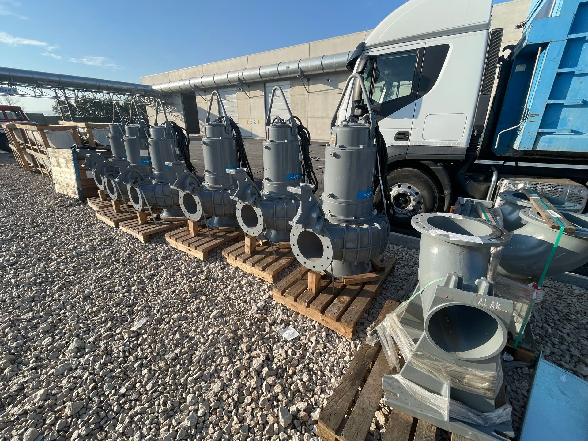 Una fila di pompe è posizionata su pallet di legno davanti a un camion.