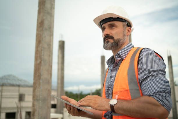 Construction worker wearing a hard hat and vest, holding a tablet at a construction site