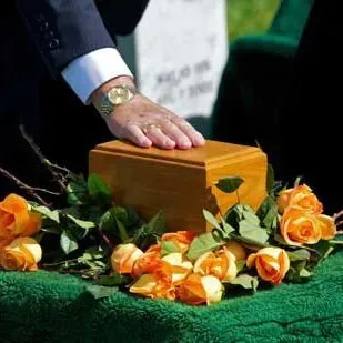 A man is putting his hand on a wooden box surrounded by flowers.