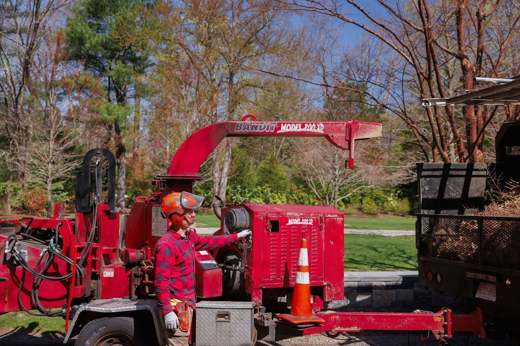A man is driving a red truck with a tree chipper attached to it.