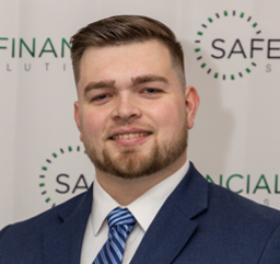 Man in a suit smiles, standing in front of a backdrop with the words