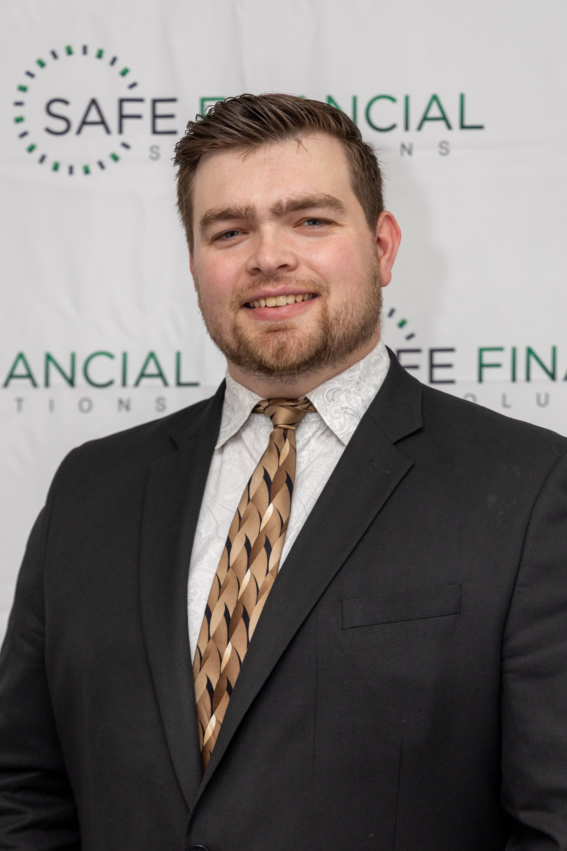 Man in a blue suit smiles at the camera, in front of a logo.