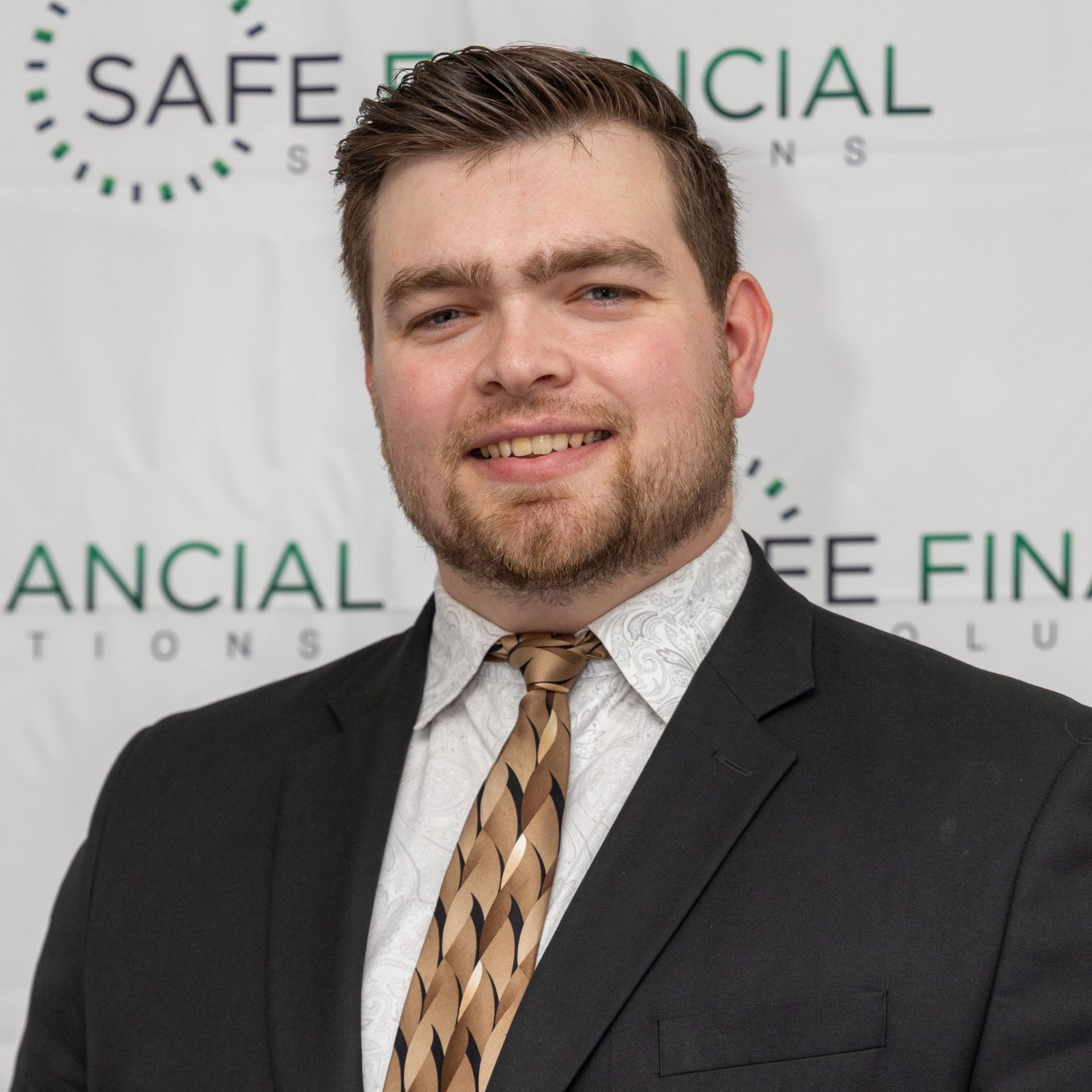 Man in a suit smiles, standing in front of a backdrop with the words 