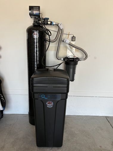 Black water softener system with tank and tubing against a wall on a garage floor