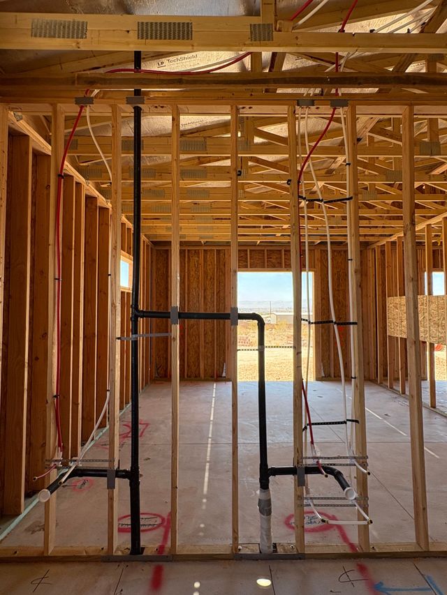 Framed interior of a house under construction with exposed wooden studs and plumbing pipes.