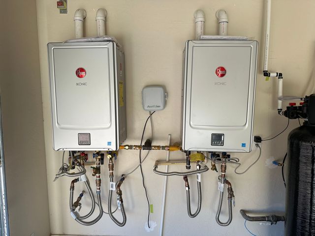 Two wall-mounted white tankless water heaters with pipes and valves in a utility room