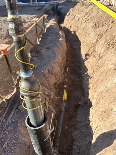 Open trench with exposed utility pipe and yellow wire at a construction site