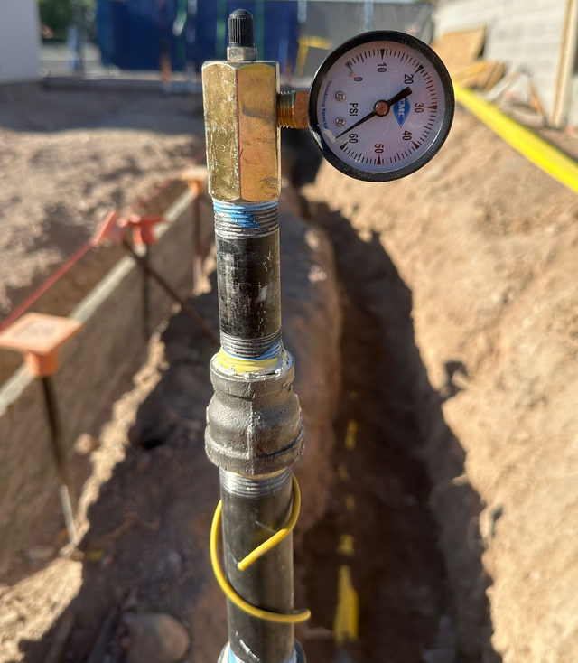 Pressure gauge on a pipe in a trench with yellow cord and construction dirt around it