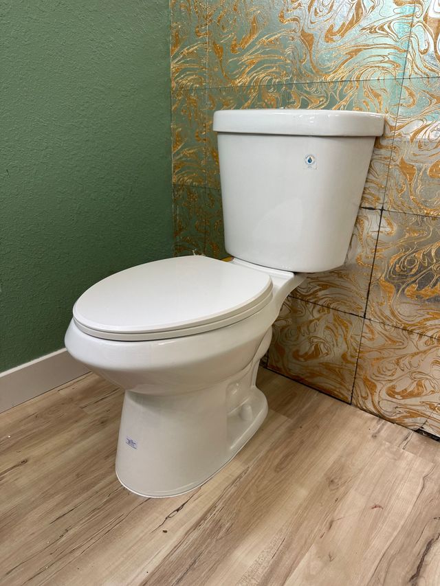 White toilet with tank in a bathroom with green and tan tiled walls and wood-look floor