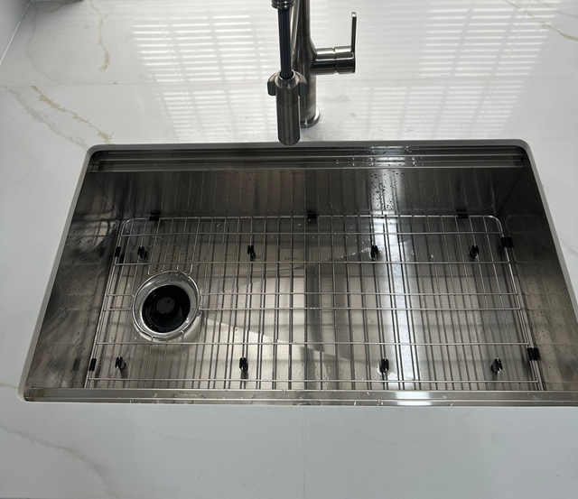 Stainless steel kitchen sink with faucet and drainboard in a white countertop.