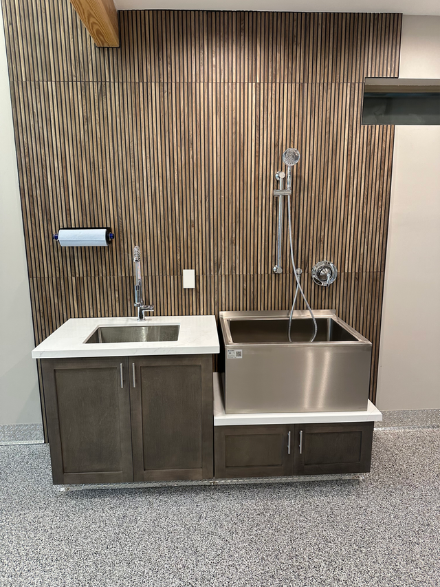 Modern kitchen sink area with white sink and stainless steel basin against a textured wood wall