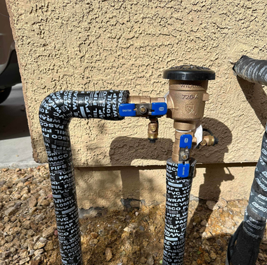 Outdoor water piping with blue shutoff valves and black insulated hoses against a stucco wall