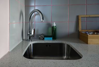 Kitchen sink with chrome faucet, soap, sponge, and dish rack on a speckled countertop.