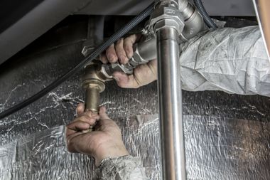 Hands tightening a pipe fitting under a sink with water spraying nearby