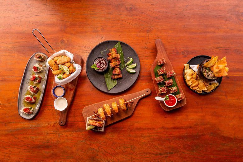 Aperitivos e bebidas variados dispostos sobre uma mesa de madeira, fotografados de cima.