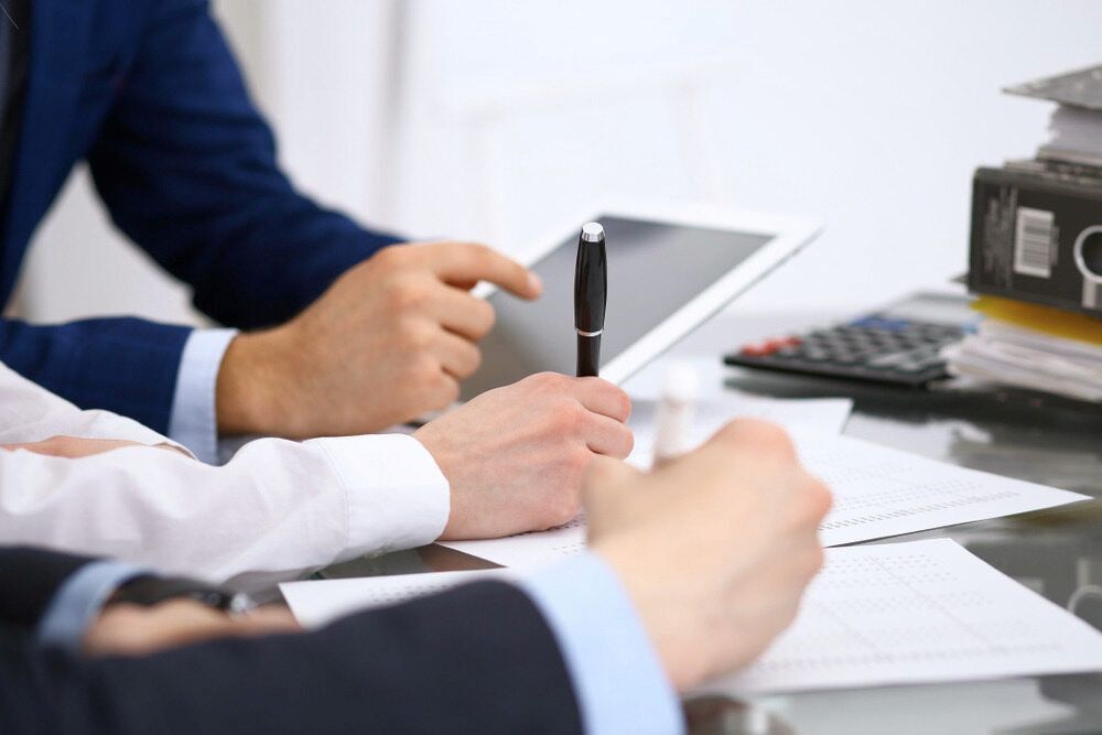 People Reviewing Documents at a Desk; One Using a Tablet, Another Writing With a Pen — NR Bookkeeping in Lennox Head, NSW