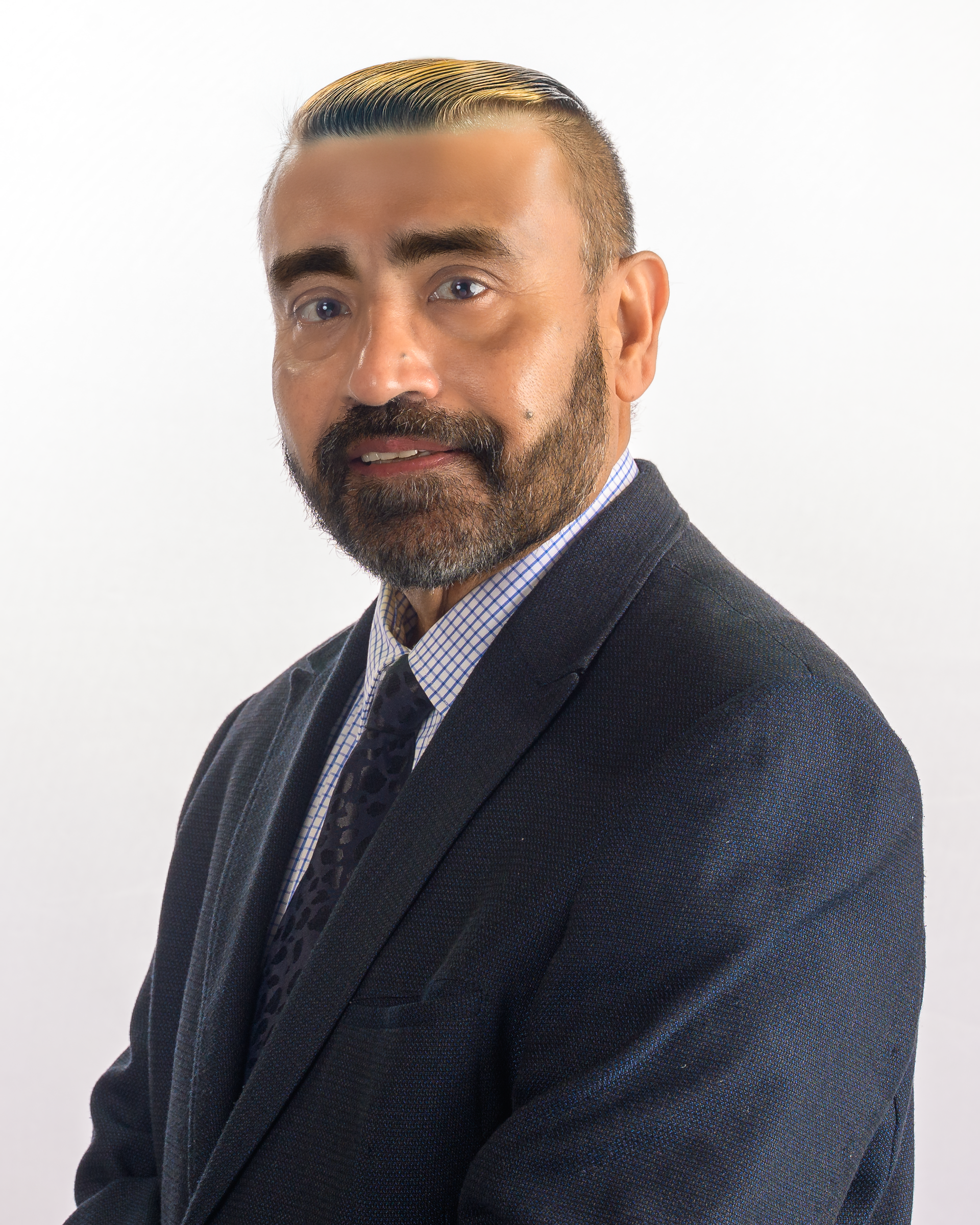 Man in a gray suit and glasses smiles, posing in front of a dark gray backdrop.