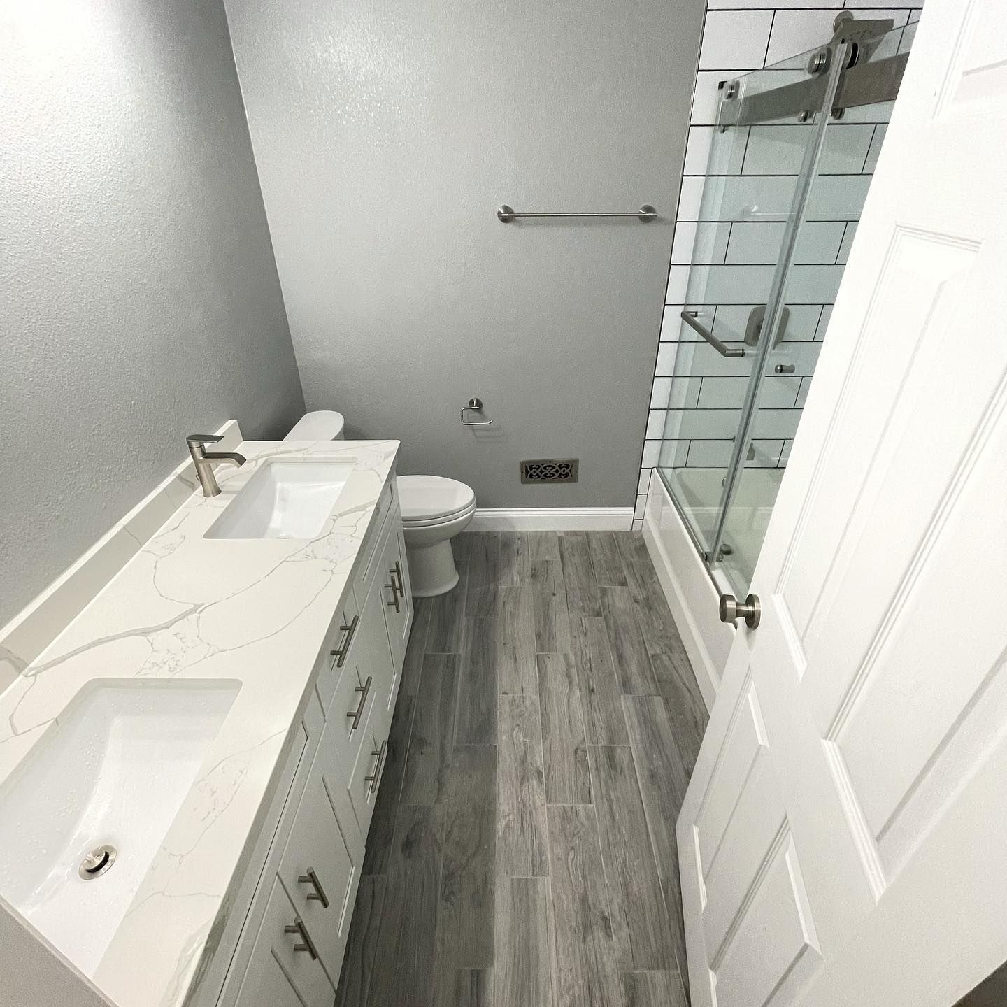 Bathroom with gray tile floor, white vanity with two sinks, toilet, and glass shower door.