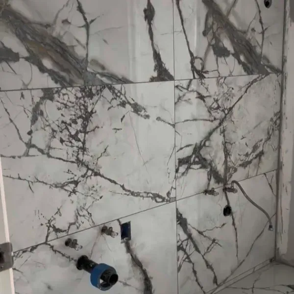 White and gray marble tile bathroom wall with plumbing fixtures installed.