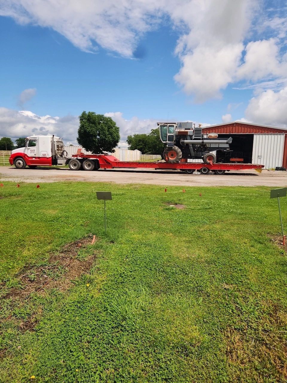 A red truck is carrying a tractor on a trailer.