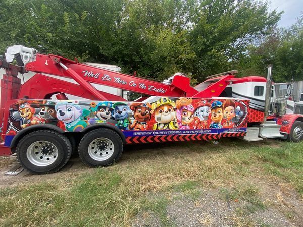 A tow truck with paw patrol characters painted on it is parked in a grassy field.