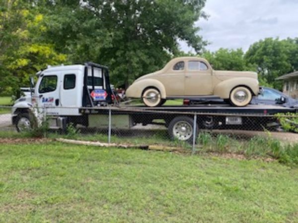 An old car is being towed by a tow truck.