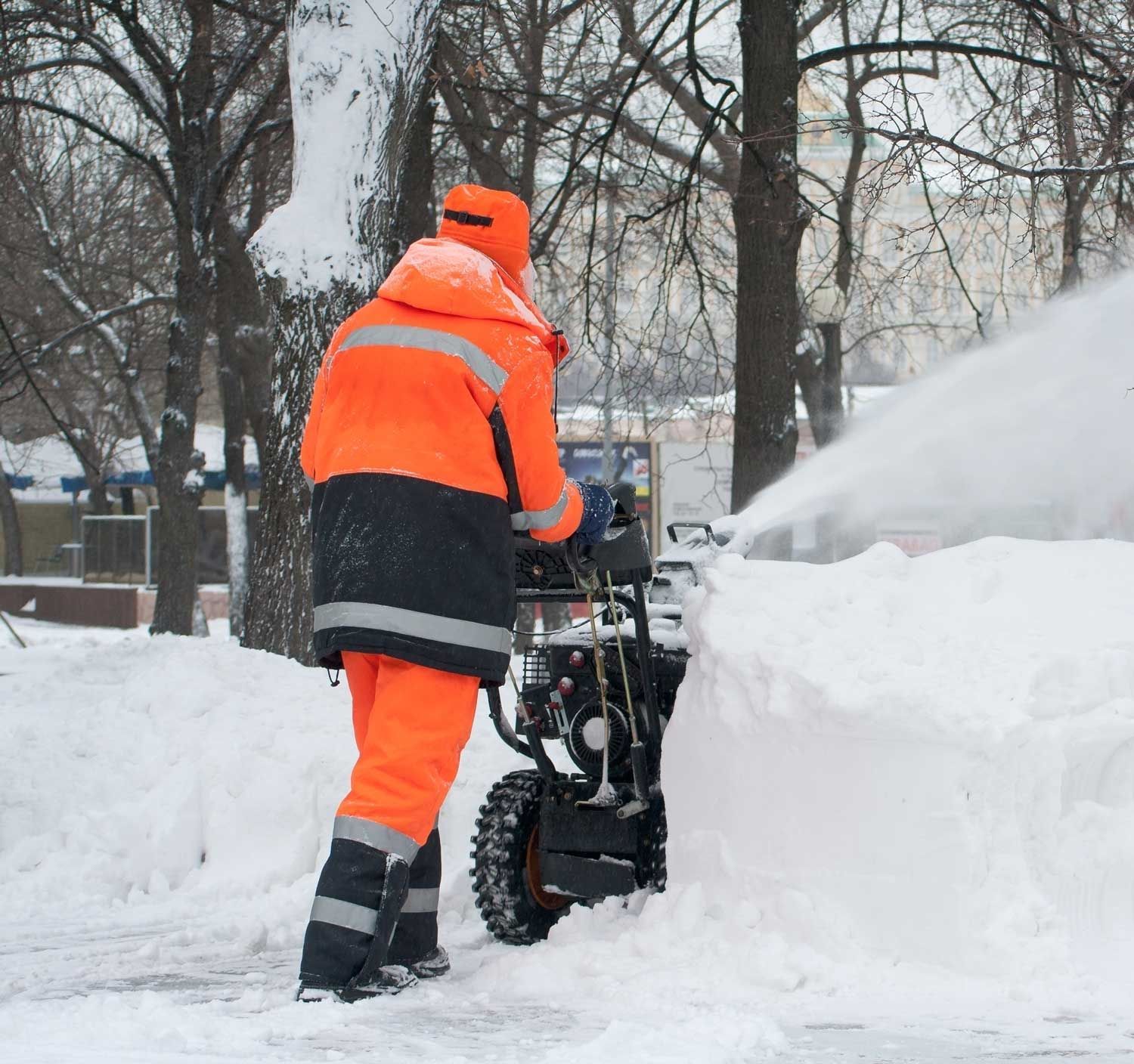 A man in an orange jacket is using a snow blower