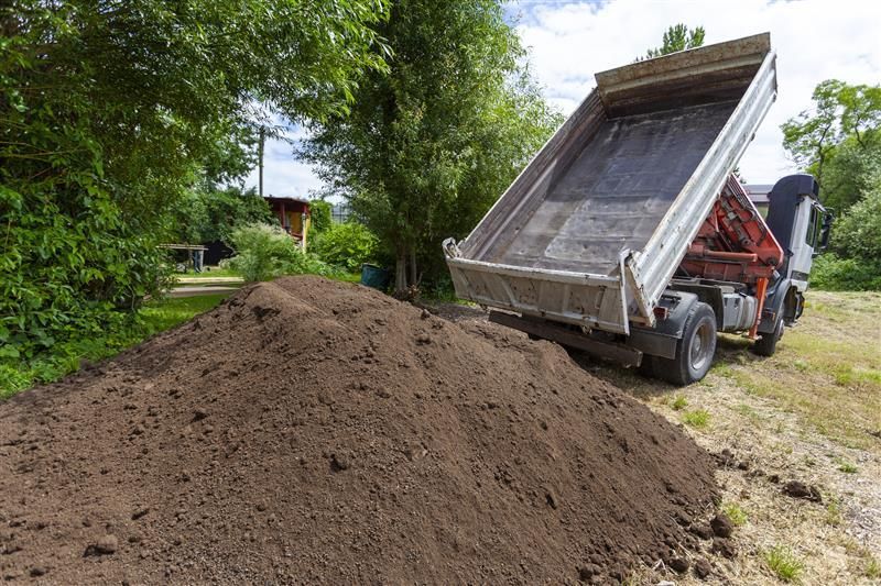 A person is carrying a wheelbarrow full of dirt in a garden.