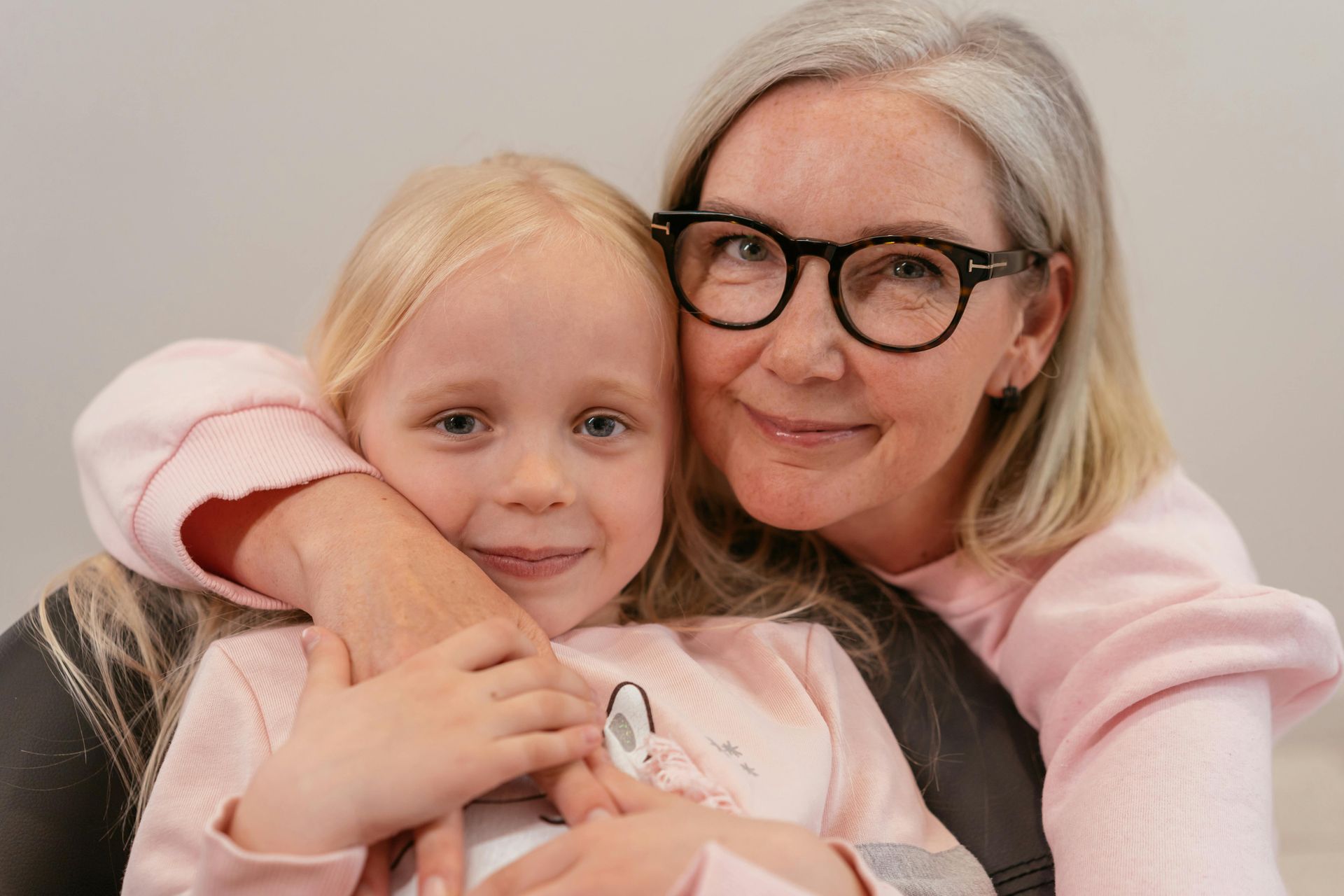 A woman wearing glasses is hugging a little girl.
