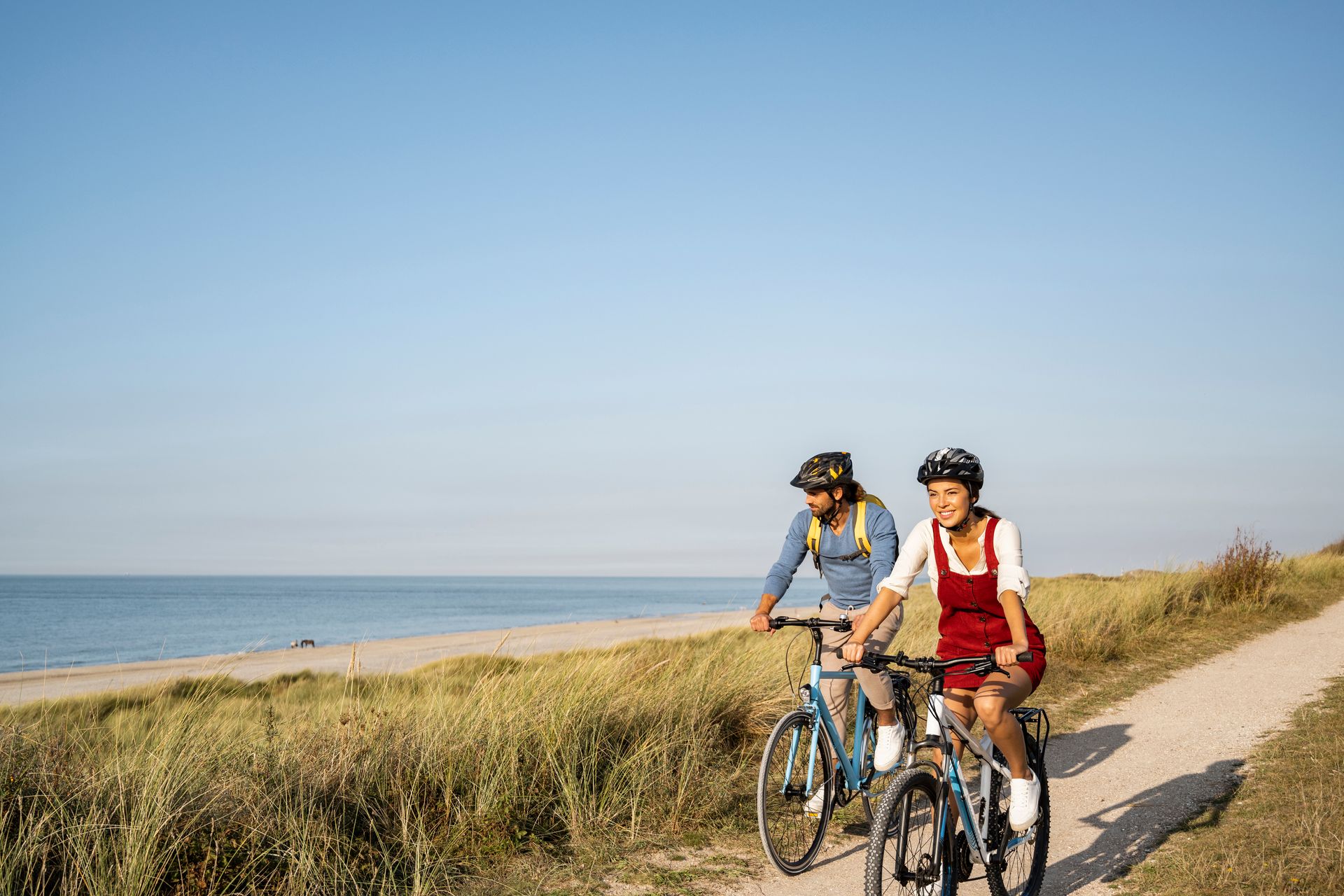 Un uomo e una donna stanno andando in bicicletta su un sentiero sterrato vicino all'oceano.