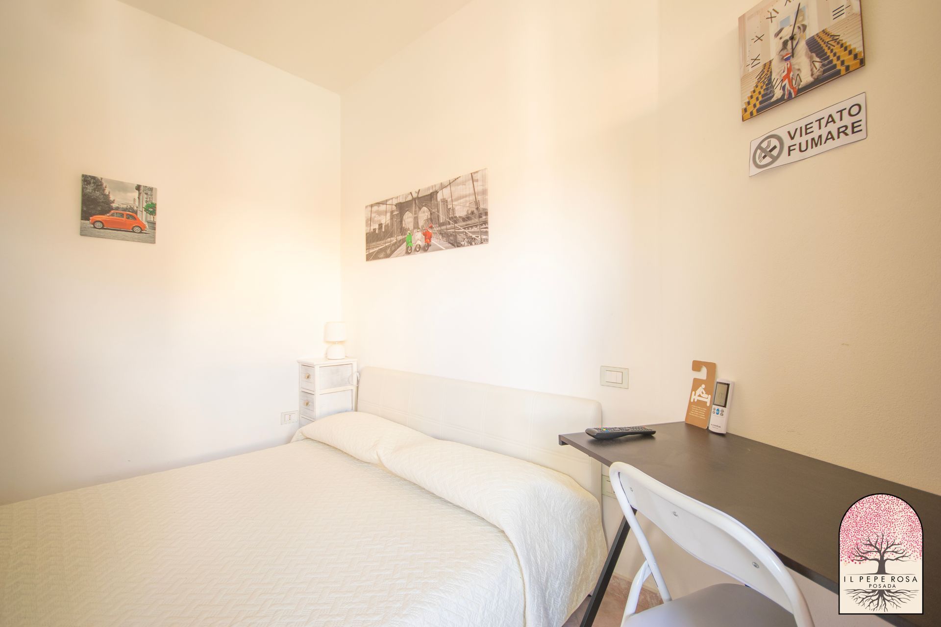 Una camera da letto con un letto, una scrivania, una sedia e quadri alle pareti.