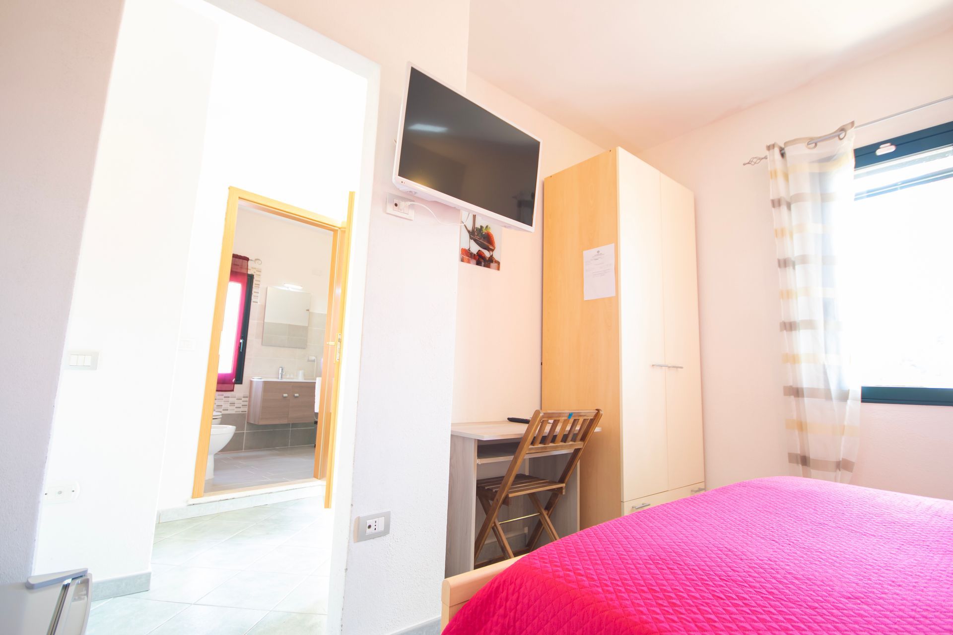 Una camera da letto con un letto, una scrivania, una televisione e uno specchio.