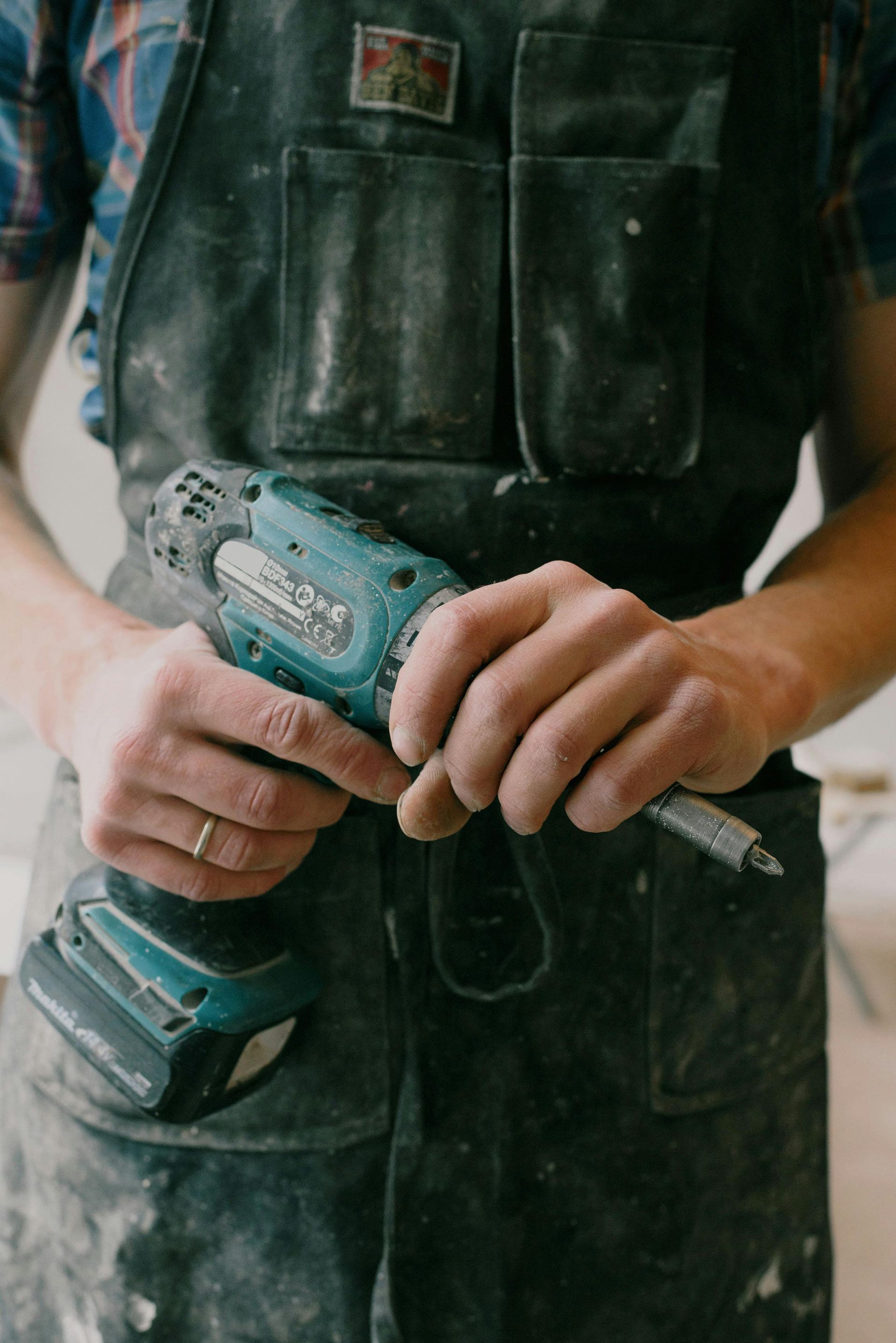 Person in apron holding a teal and black drill.