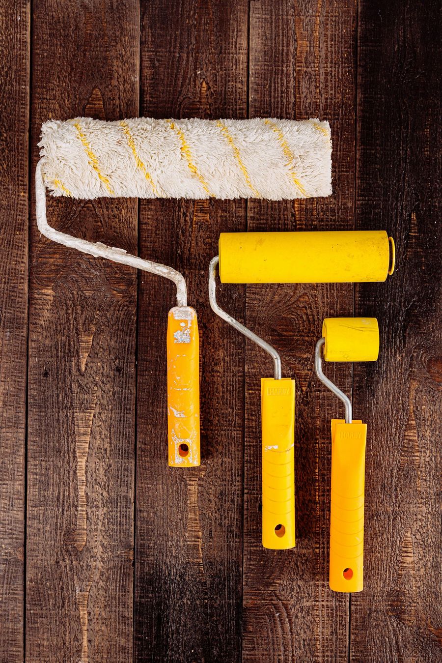 Three yellow paint rollers on a dark wood surface. The largest is at the top.