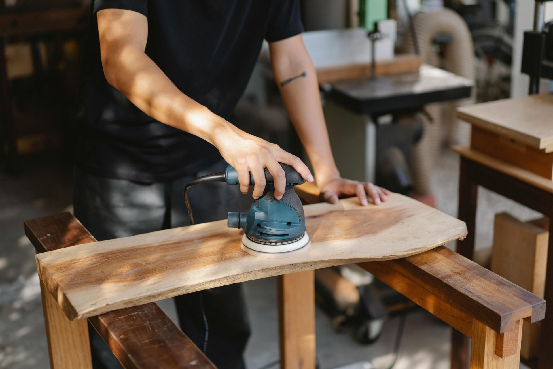 Person sanding a wooden board with a power sander in a workshop.