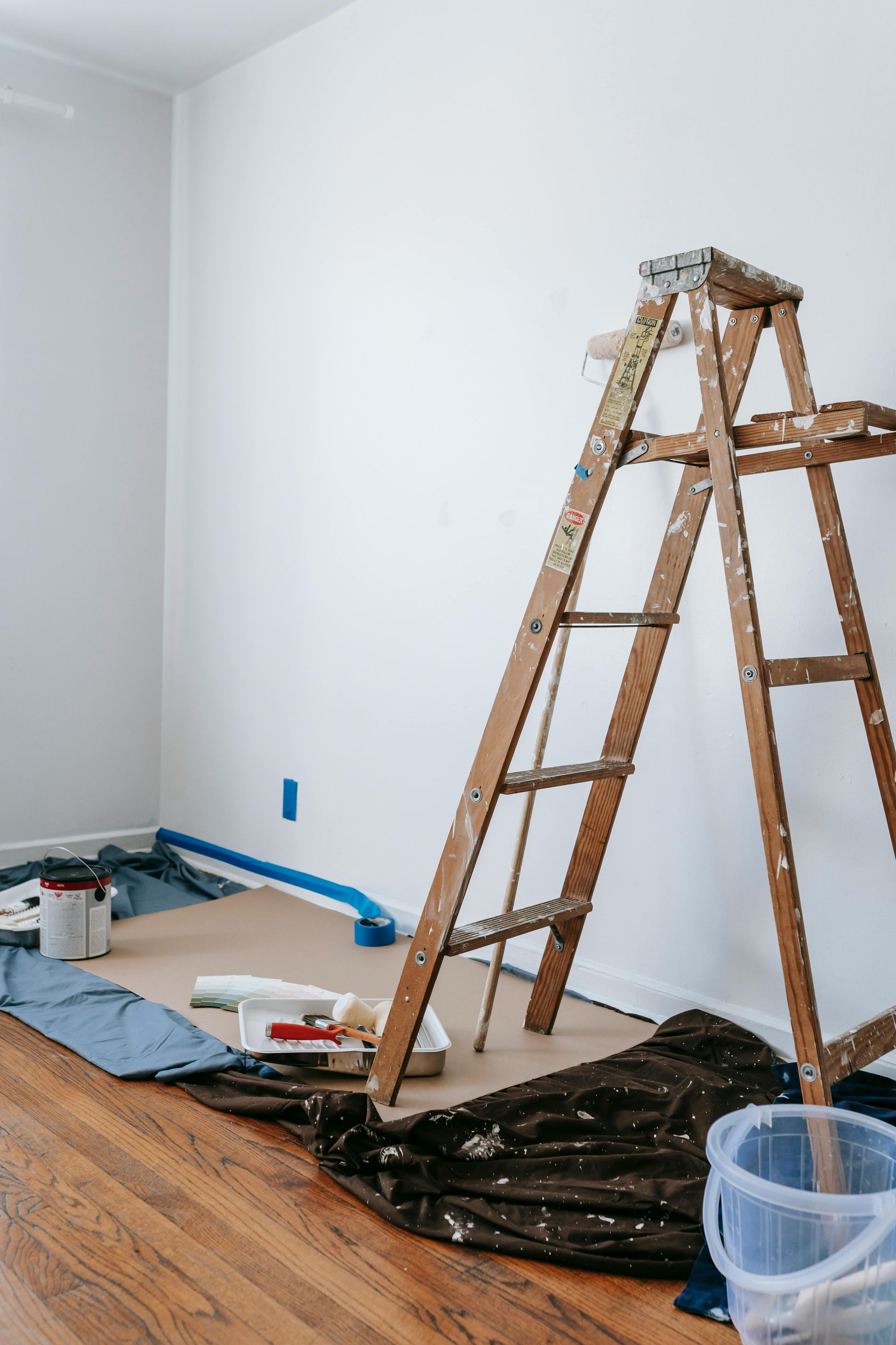 Wooden ladder and painting supplies in room being painted white.